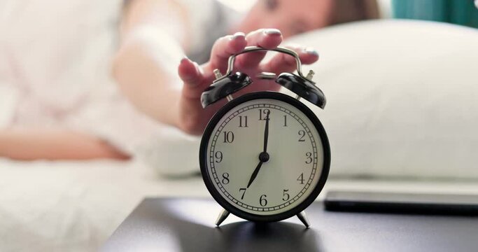 The woman turns off the ringing alarm clock and continues to sleep