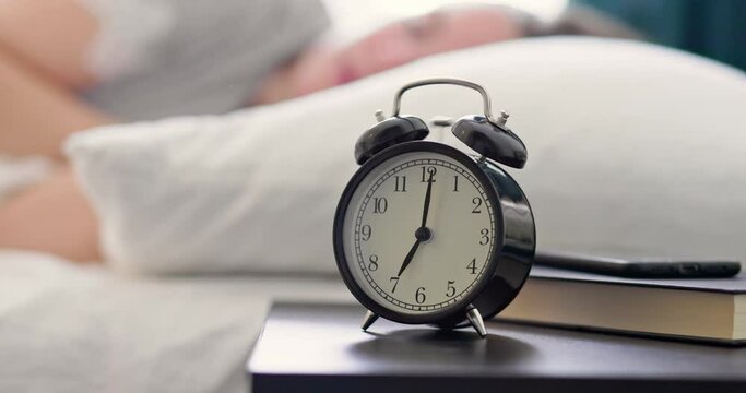 Tired woman ignores the ringing alarm clock.  Alarm clock is ringing to wake up a woman sleeping in bed