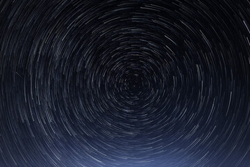 Stellar trails, the rotation of bright stars at night around the Polar Star against a blue sky and a meteor