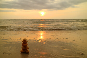 Closeup stack of balanced pebble stones on the sunset beach against splashing waves 