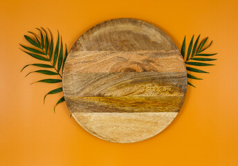 Green palm branches and wooden tray over orange background. Flat lay, top view, copy space. Mock up