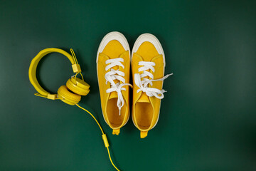 Yellow sneakers and headphones on green background. Trendy background. Mock up, summer holidays, vacation, travel, fashion, music concept