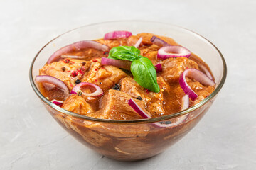 Raw meat marinated with bbq sauce, pepper, onion and basil in a bowl on white background. Marinating meat for cooking barbecue
