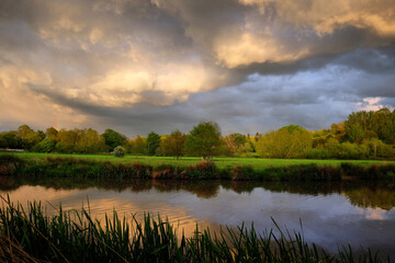 Fototapeta na wymiar Stormy skies as the sun sets over the River Wey and meadows in Godalming, Surrey, UK