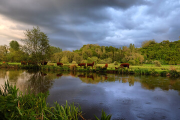 Fototapeta na wymiar Stormy skies as the sun sets over the River Wey and meadows in Godalming, Surrey, UK