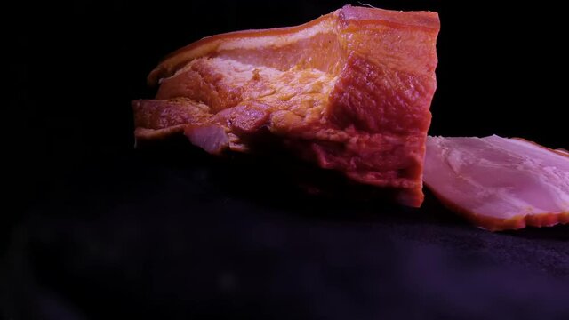 Rotating a large piece of loin and chopped pieces on a dark background. Looped video.