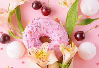 pink donat and fresh cherries, alstroemeria flowers in a paper envelope on a pink
