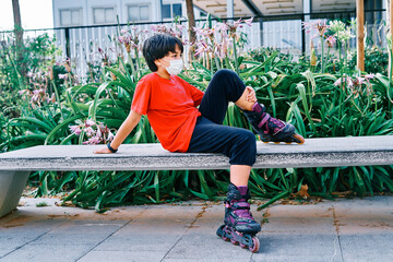 Caucasian boy sitting on a bench with roller skates in the park.