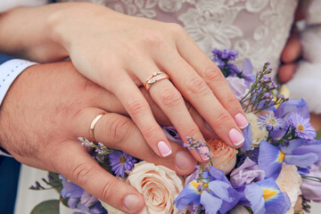 Fototapeta premium hands of the newlywed with gold wedding rings on the background of a bouquet of blue irises and beige roses, the bride and groom,