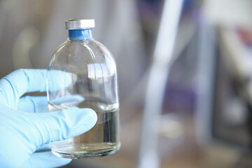 Researcher hand wearing gloves holding a bottle for anaerobic cultures, with cap and septum. Anaerobic media.