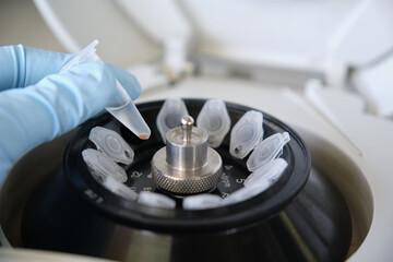 Close up of a researcher hand with glove holding a small eppendorf tube with a pellet over a mini...