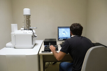 Young man scientist working with scanning electron microscope. Laboratory technician observing...