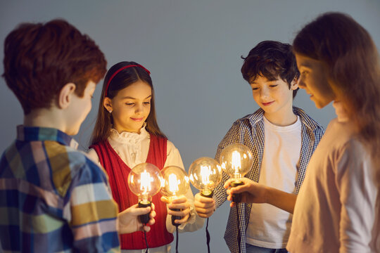 Collective thinking, team work and innovation. Smart school children joining idea brain light bulb together standing in circle looking at glowing lamp studio shot on grey background