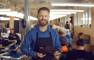 Portrait of footwear factory worker with brand new product. Happy young man standing in workshop,...