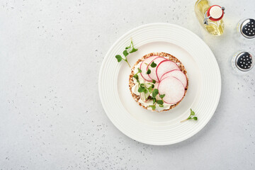Crispy buckwheat bread cake gluten free with cream cheese, red radish and microgreen for healthy breakfast on grey stone background. View from above. Concept vegan and healthy eating.