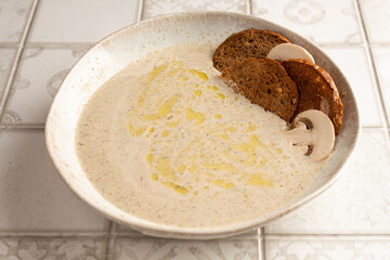 cream soup of champignons on a tiled table with bread chips