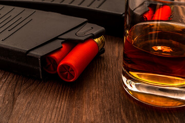 Two magazines with red cartridges 12 gauge and glass of whiskey on the wooden table. Close up view