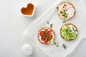Three crispy buckwheat bread gluten free with cream cheese, radish, tomato, cucumber and microgreen for healthy breakfast on parchment paper on stone background . Concept vegan and healthy eating.