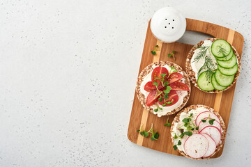 Three crispy buckwheat bread  gluten free with cream cheese, radish, tomato, cucumber, and microgreen for healthy breakfast on wooden stand on grey stone background. Concept vegan and healthy eating.