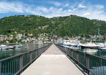 Fototapeta na wymiar pedestrian walkway crosses the port of como, in the background the mountain with the funicular to Brunate. Lombardy, northern Italy.