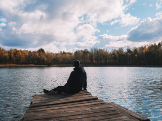 A young man on a wooden bridge by the lake, on a gloomy autumn day. The atmosphere of loneliness and sadness