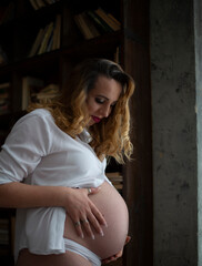 happy pregnant woman eighth ninth month of pregnancy hugging her belly with her hand and looks at...