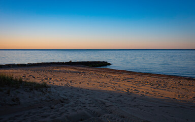 Peaceful seascape over the jetty and sandy beach on Cape Cod. Sunrise at dusk over Martha's Vineyard with clear blue sky and calm seawater.