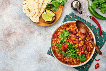 Mexican black bean soup with minced meat, tomato, cilantro, avocado and vegetables stew on a light grey slate, stone or concrete background. Traditional Mexican dish. Top view with copy space.