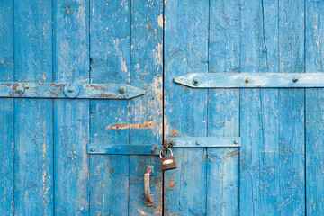 Wooden background. Old blue shabby wooden door with iron fasteners and a rusty lock. Torn up...