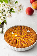Delicious sweet apple pie in a round baking dish, blossoming apple tree branches