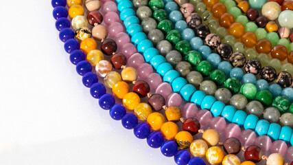 Multicolored beads made of natural stones are laid out on the white background.  Flat lay. Natural...