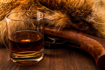 Hunting rifle with glass of whiskey lying next to the animal's fur produced. View close-up, focus...
