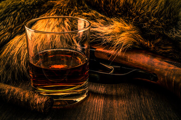 Hunting rifle with glass of whiskey and cuban cigar lying next to the animal's fur produced. View...