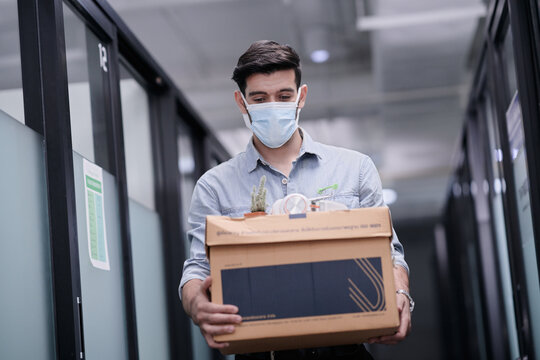 A man, holding a box containing his belongings, is walking out of office after received termination notification from his manager.
