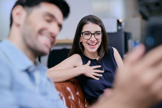 A happy businesswoman is watching something on her friend's smartphone with big smile on her face.