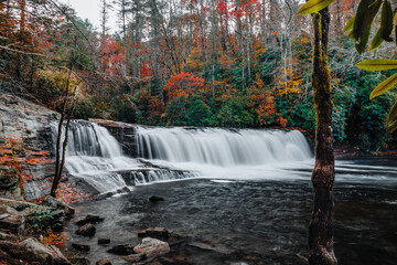 Hooker Falls, a waterfall of the Little River surrounded by colorful fall foliage on a gloomy, cloudy day in DuPont State Recreational Forest, Hendersonville, North Carolina, USA. Long exposure.