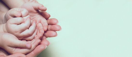 Female hands hold baby hands, banner with place for text and advertising. The concept of protecting...