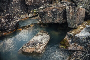 Scenic nature background of turquoise clear water stream among rocks with mosses and lichens. Atmospheric mountain landscape with mossy stones in transparent mountain creek. Beautiful mountain stream.