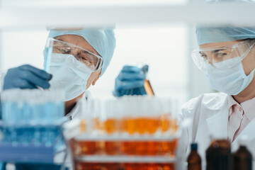 scientists in protective masks standing in front of a rack of test tubes .