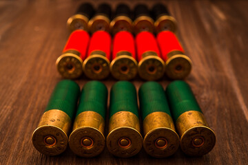 Three rows of 12 gauge cartridges lying on a wooden table. Focus on the green cartridges