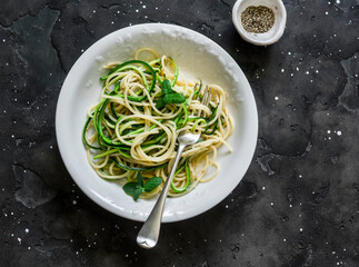 Vegetarian pasta - spaghetti with zucchini, lemon zest and mint on a dark background, top view
