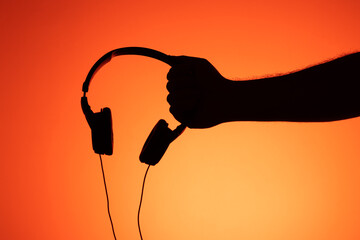 Hand holding a headset headphones on an orange background.