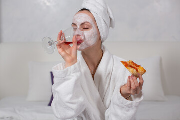 portrait of a girl in a white robe and a moisturizing face mask, who drinks red wine from a glass,...