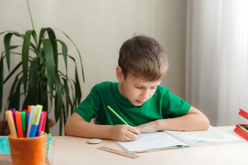 7 years old child boy doing lessons sitting at desk in his room. Kid writing homework in notebook