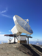 Huge white antenna radio telescope on blue sky background on top of the mountain