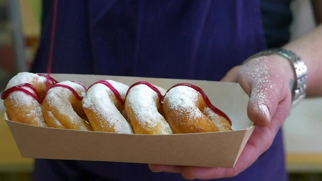 Strawberry topping pours donuts. Paper box with donuts set on lilac apron background closeup. 