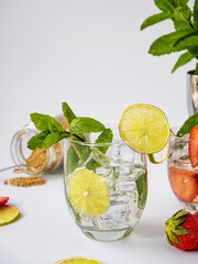 Glass with strawberry, lime, ice and mint. Mojito with cane sugar. White bottom. Refreshing summer drink. A feeling of freshness.