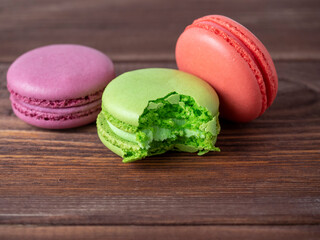 Colorful macaroons on a brown wooden background. One of them is bitten off. Delicious dessert