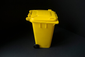 Contenedor amarillo para plásticos sobre cartulina negra. Reciclaje de plástico