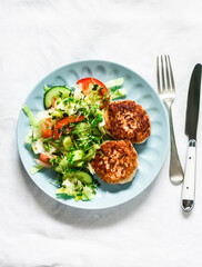 Chicken burgers and fresh iceberg, tomatoes, cucumber salad on a light background, top view